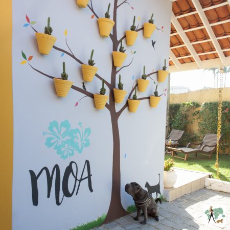 cachorro sentado ao lado de parede com a pintura de uma árvore